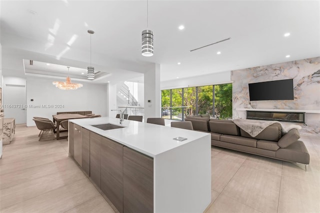 kitchen featuring sink, a chandelier, a raised ceiling, hanging light fixtures, and a center island with sink