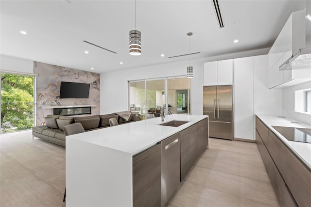 kitchen featuring sink, decorative light fixtures, wall chimney exhaust hood, stainless steel appliances, and a center island with sink