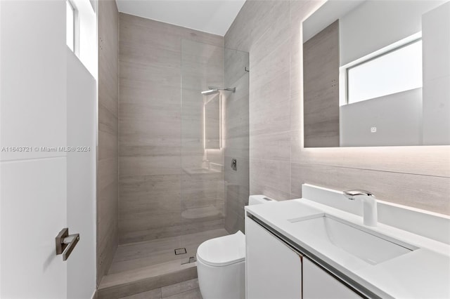 bathroom with toilet, tiled shower, vanity, and tile walls