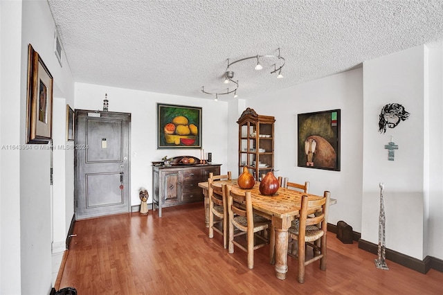 dining space featuring rail lighting, wood-type flooring, and a textured ceiling