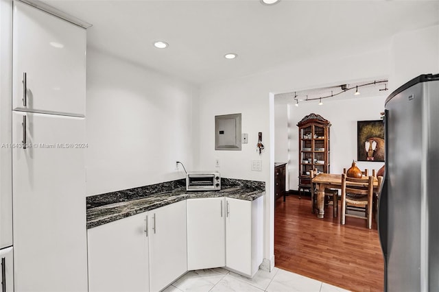 kitchen featuring light tile patterned flooring, stainless steel refrigerator, dark stone counters, and electric panel