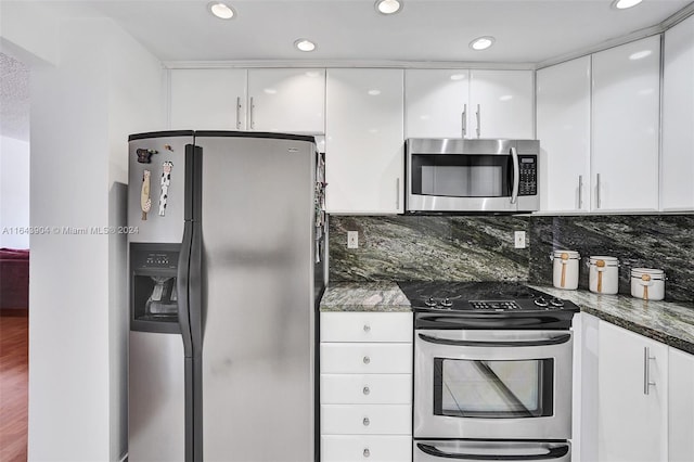 kitchen with stainless steel appliances, decorative backsplash, white cabinetry, dark stone countertops, and hardwood / wood-style flooring