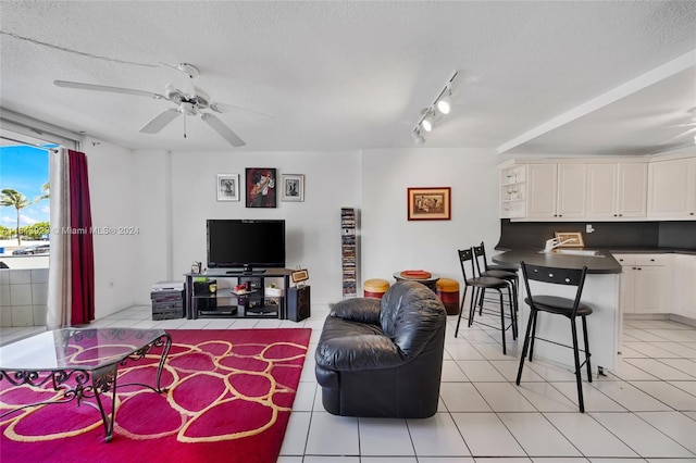 living room with ceiling fan, track lighting, light tile patterned floors, sink, and a textured ceiling