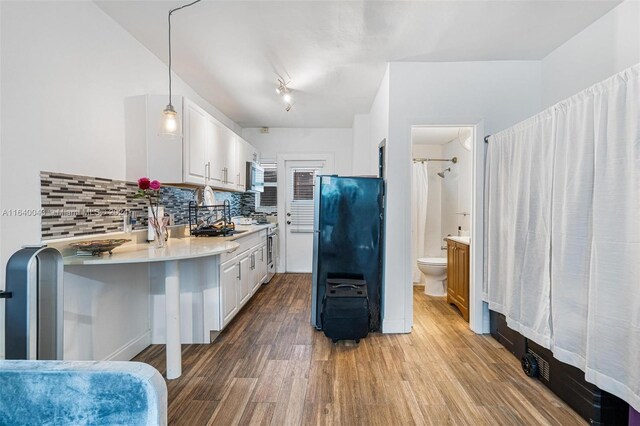 kitchen with backsplash, black refrigerator, hardwood / wood-style flooring, white cabinetry, and hanging light fixtures