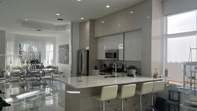 kitchen featuring a tray ceiling, kitchen peninsula, appliances with stainless steel finishes, sink, and a breakfast bar area