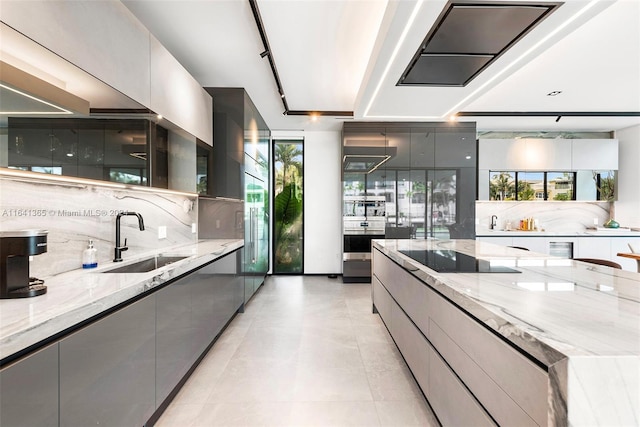 kitchen featuring sink, plenty of natural light, black electric stovetop, light stone counters, and gray cabinets