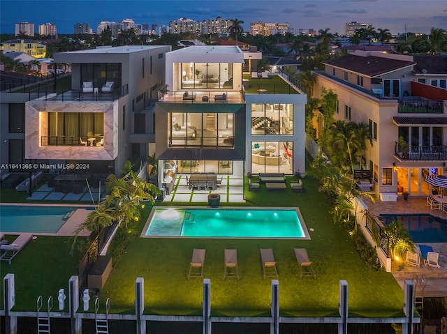 back house at dusk featuring a balcony, a fenced in pool, and a patio area