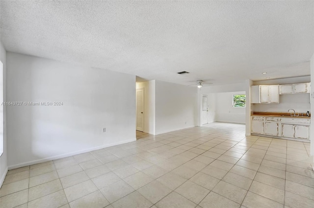 unfurnished living room with a textured ceiling, ceiling fan, sink, and light tile patterned floors