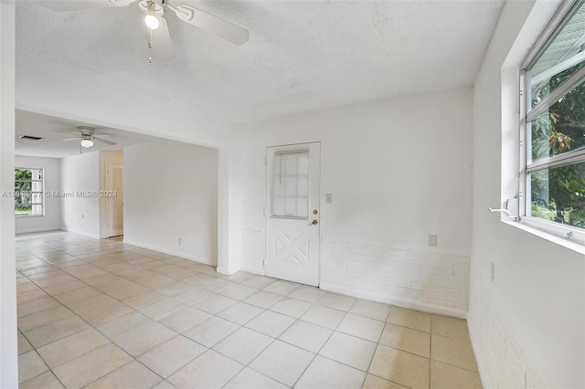 empty room with ceiling fan, light tile patterned floors, and a textured ceiling