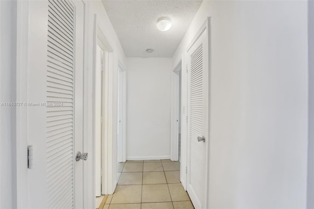 corridor with a textured ceiling and light tile patterned flooring