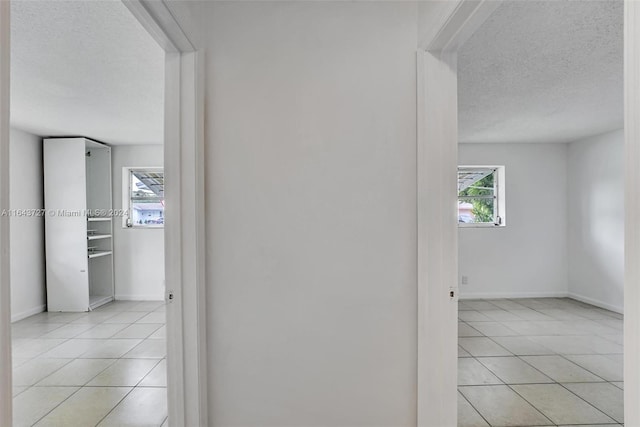 hall with a textured ceiling, plenty of natural light, and light tile patterned floors