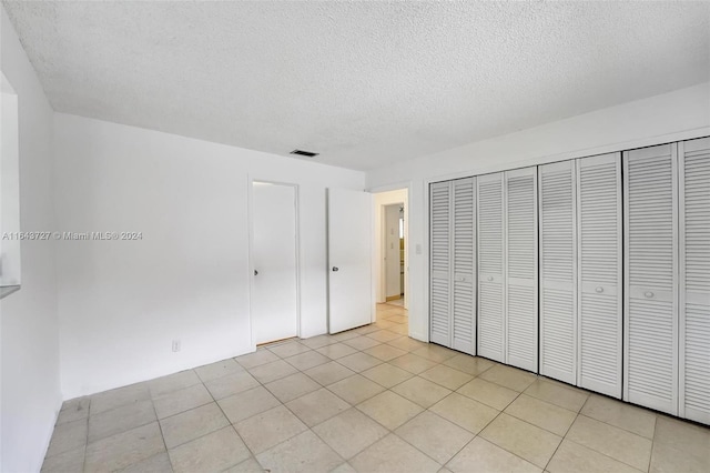 unfurnished bedroom featuring a textured ceiling, light tile patterned flooring, and a closet