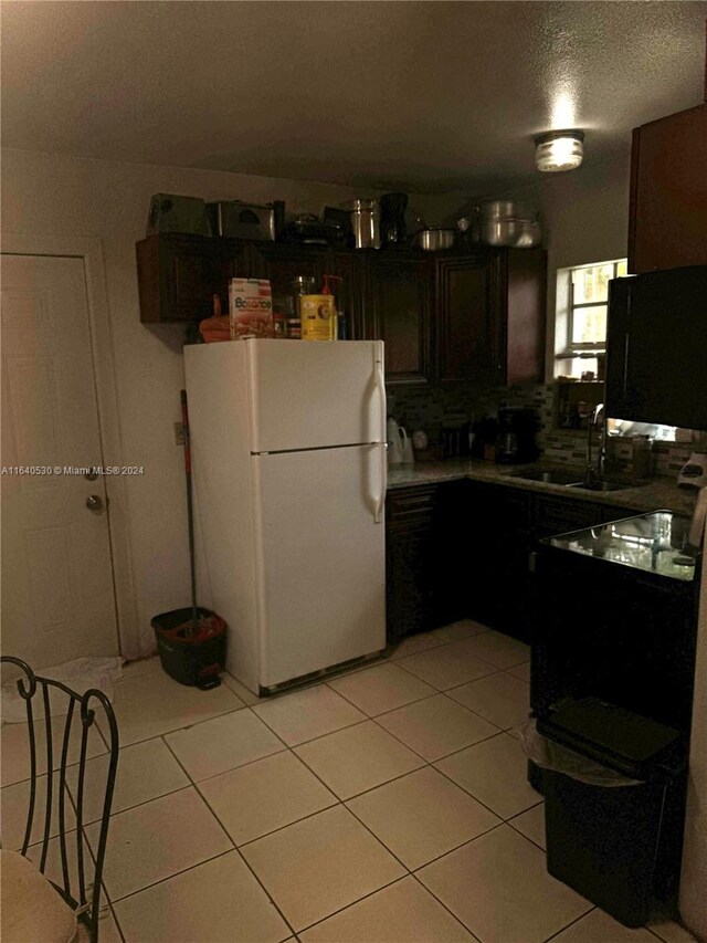 kitchen with backsplash, dark brown cabinetry, white refrigerator, light tile patterned floors, and sink