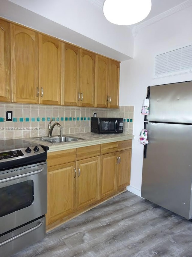 kitchen featuring tasteful backsplash, hardwood / wood-style floors, ornamental molding, appliances with stainless steel finishes, and sink