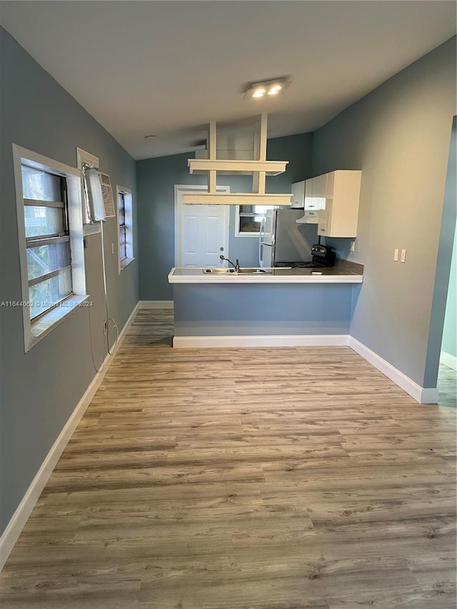 kitchen featuring light hardwood / wood-style floors, vaulted ceiling, white cabinets, kitchen peninsula, and sink