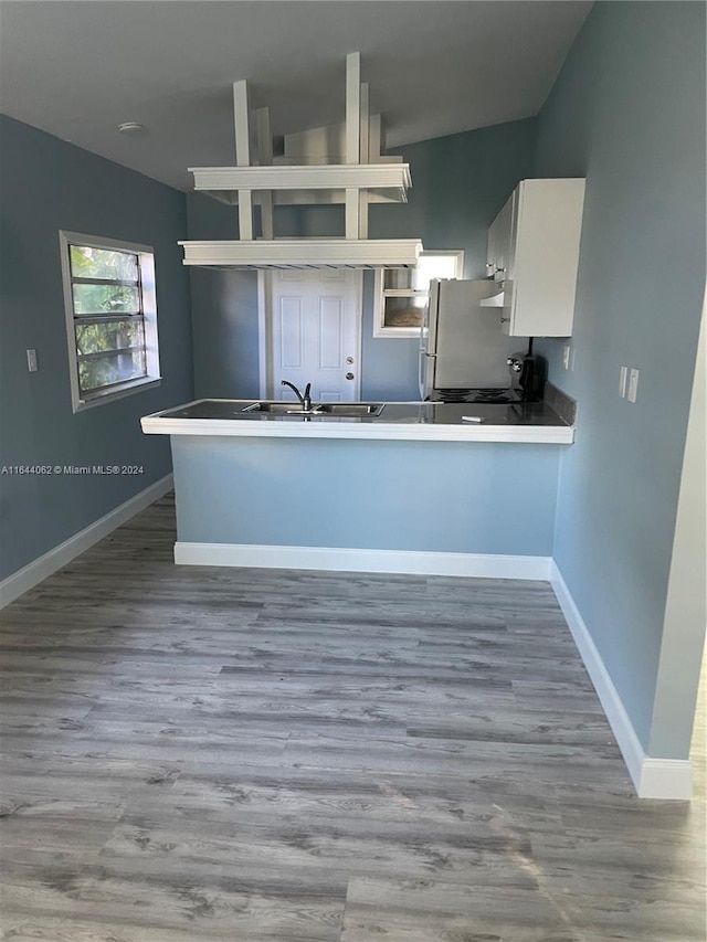 kitchen featuring wood-type flooring, kitchen peninsula, white cabinetry, and white fridge