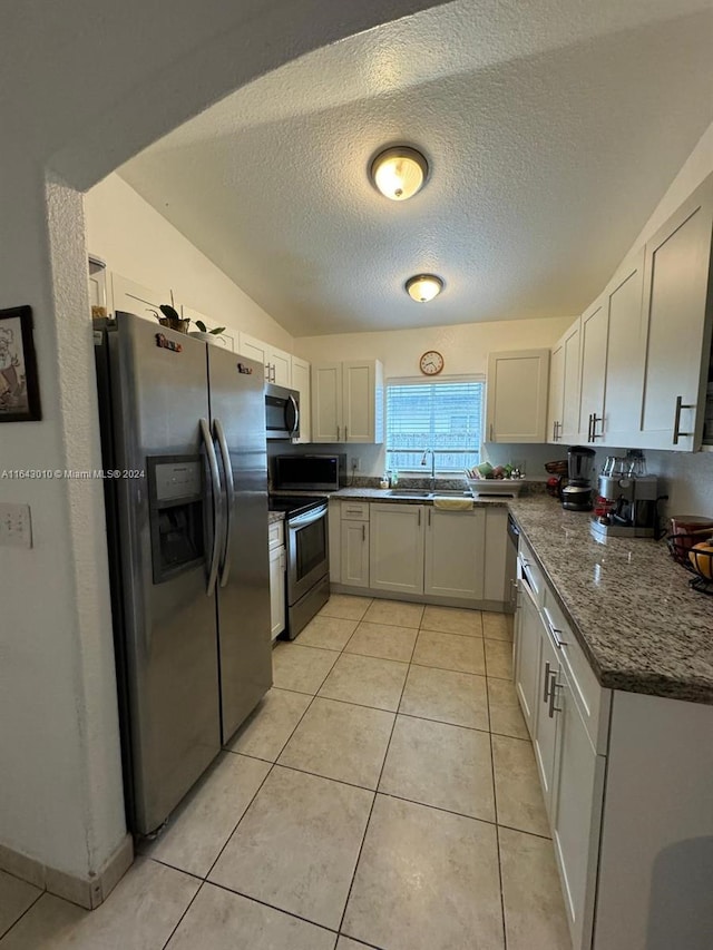 kitchen featuring sink, a textured ceiling, light tile patterned floors, stainless steel appliances, and white cabinets