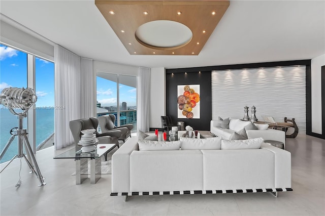 living room featuring light tile patterned floors, a raised ceiling, floor to ceiling windows, and a water view