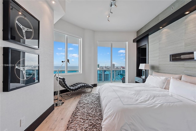 bedroom with access to outside, track lighting, a water view, and wood-type flooring