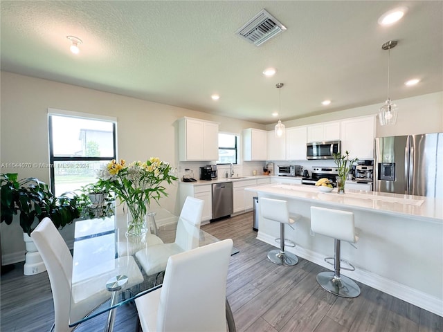 kitchen featuring stainless steel appliances, a sink, visible vents, white cabinets, and pendant lighting