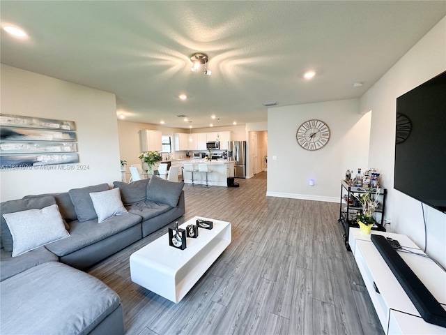 living room featuring light wood finished floors, recessed lighting, and baseboards