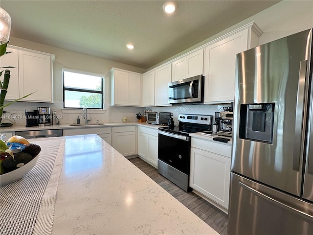 kitchen with light stone counters, appliances with stainless steel finishes, white cabinets, and a sink