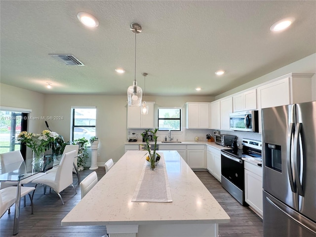 kitchen with a kitchen island, appliances with stainless steel finishes, white cabinets, and decorative light fixtures