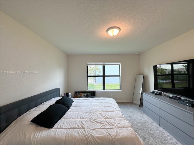 bedroom with light carpet, a textured ceiling, and baseboards