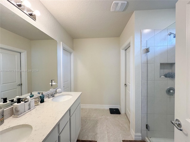 bathroom with double vanity, a stall shower, a sink, a textured ceiling, and baseboards