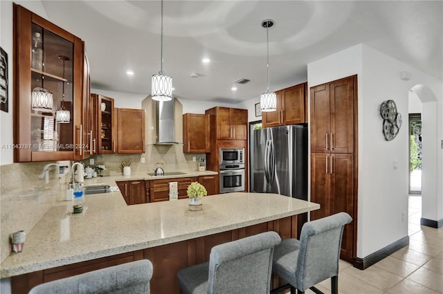 kitchen featuring sink, wall chimney exhaust hood, kitchen peninsula, decorative light fixtures, and appliances with stainless steel finishes