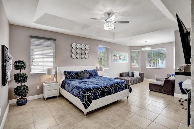 tiled bedroom with a tray ceiling, multiple windows, and ceiling fan