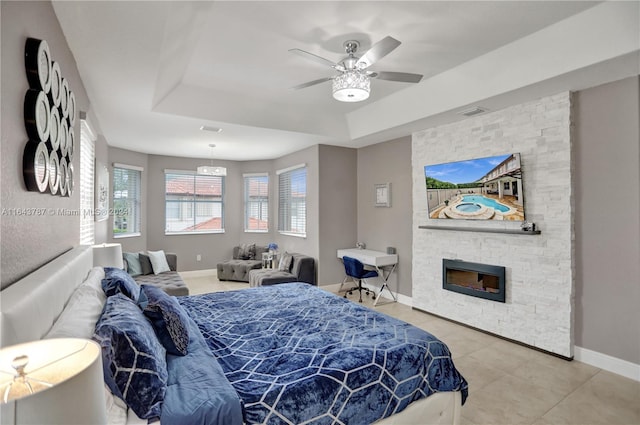 tiled bedroom featuring a raised ceiling, ceiling fan, and a fireplace