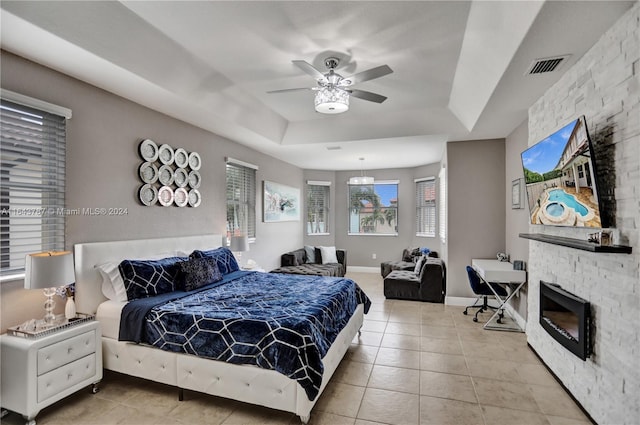 bedroom with a fireplace, a tray ceiling, ceiling fan, and light tile patterned flooring