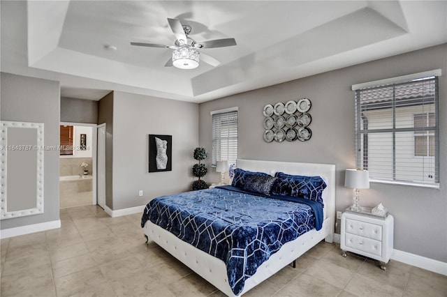 bedroom with a tray ceiling, ensuite bathroom, and ceiling fan