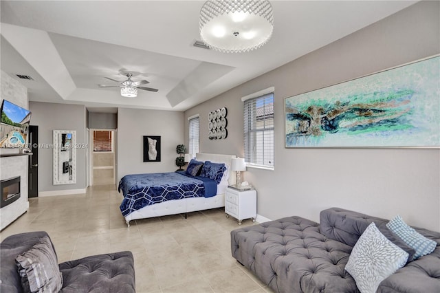 tiled bedroom featuring a large fireplace, a raised ceiling, and ceiling fan