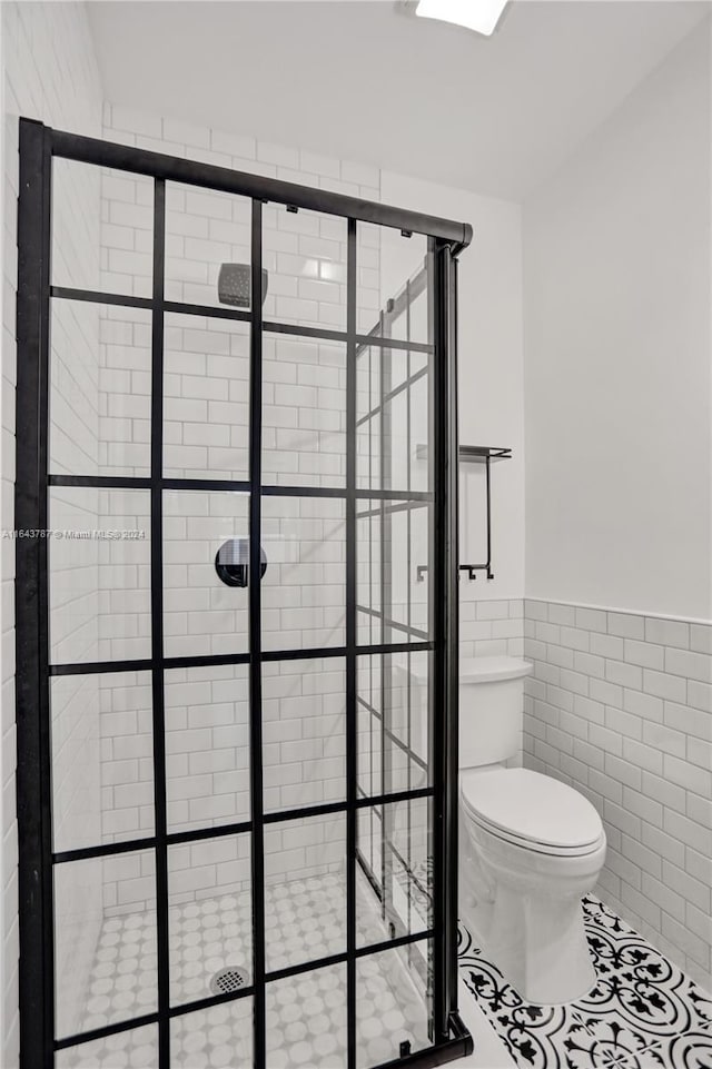 bathroom featuring tile patterned flooring, tiled shower, toilet, and tile walls