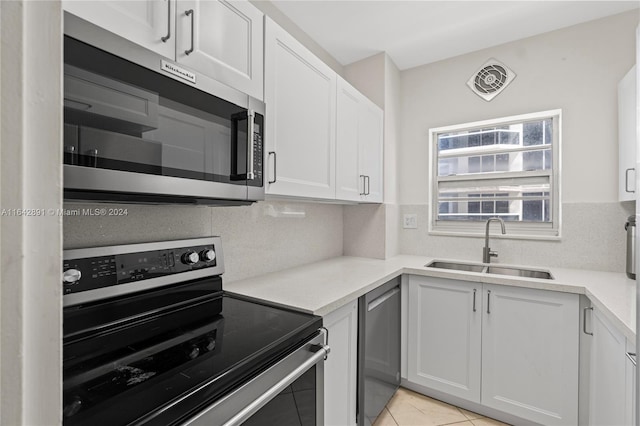 kitchen featuring tasteful backsplash, white cabinets, light tile patterned floors, sink, and stainless steel appliances