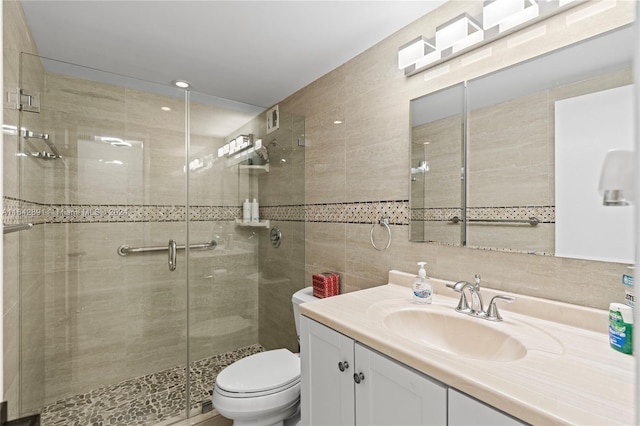 bathroom with tile walls, a shower with door, vanity, and toilet