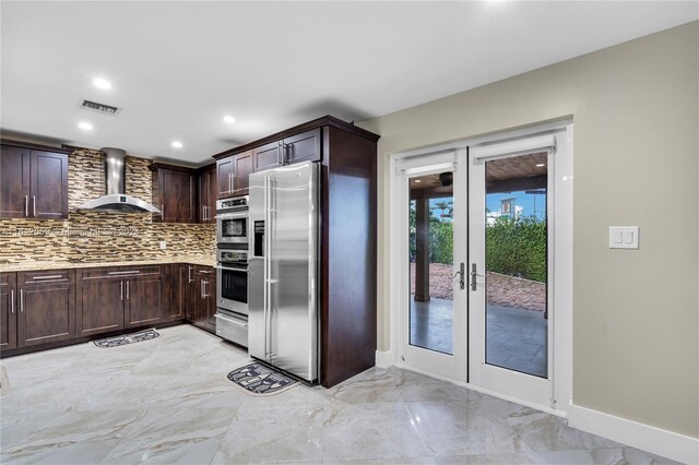 kitchen featuring backsplash, dark brown cabinets, french doors, stainless steel appliances, and wall chimney range hood