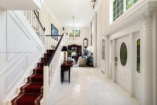 entrance foyer with a notable chandelier, a decorative wall, stairs, decorative columns, and crown molding