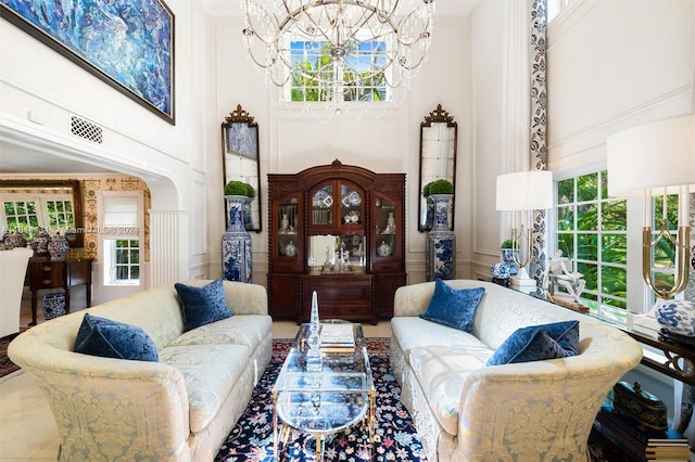 living area with arched walkways, a chandelier, a decorative wall, a towering ceiling, and ornamental molding