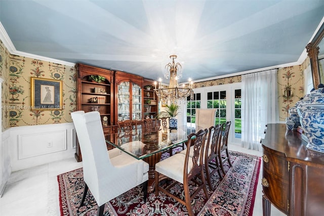 dining space with a decorative wall, an inviting chandelier, ornamental molding, wainscoting, and wallpapered walls