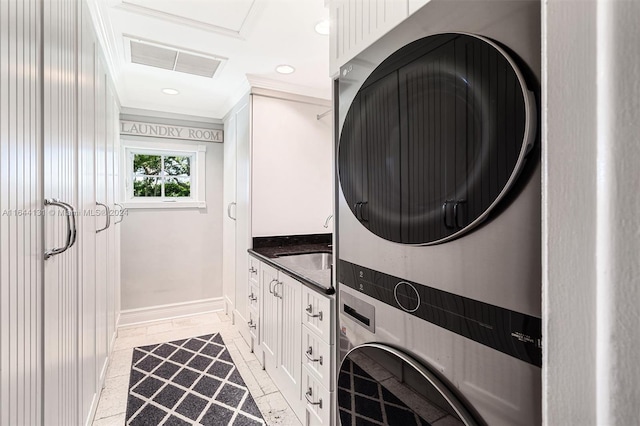 washroom with stacked washer and clothes dryer, crown molding, cabinet space, visible vents, and baseboards