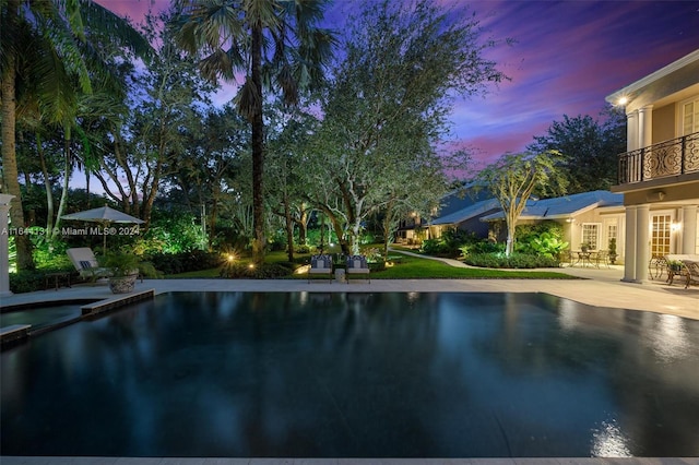 pool at dusk featuring a pool with connected hot tub and a patio