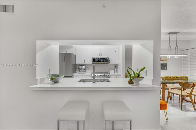 kitchen with a kitchen breakfast bar, decorative light fixtures, white cabinetry, stainless steel appliances, and kitchen peninsula