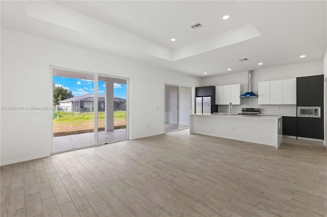 unfurnished living room with sink, light hardwood / wood-style flooring, and a tray ceiling