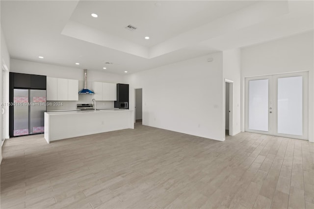 kitchen featuring white cabinetry, french doors, a kitchen island with sink, wall chimney range hood, and stainless steel fridge