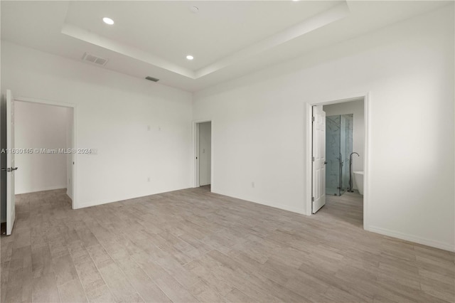 unfurnished bedroom featuring light hardwood / wood-style floors, a raised ceiling, and connected bathroom