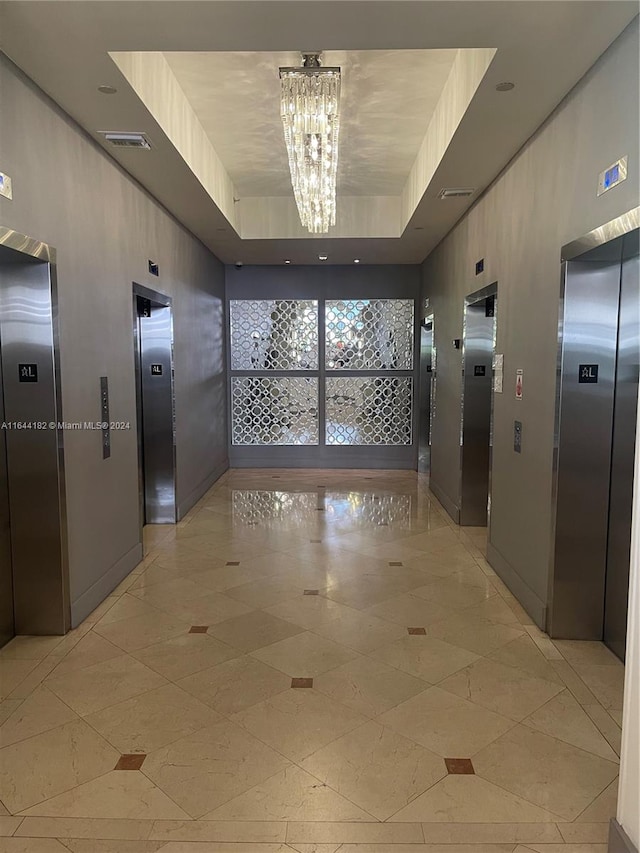 hallway with a notable chandelier, a tray ceiling, and elevator