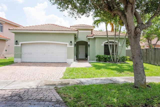 mediterranean / spanish house featuring fence, stucco siding, a garage, a tiled roof, and decorative driveway